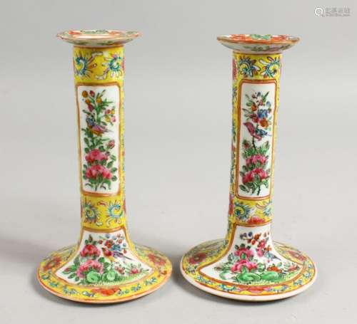 A GOOD PAIR OF CANTON FAMILLE JAUNE CANDLESTICKS with panels of flowers and birds. 7ins high.