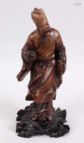 A JAPANESE MEIJI PERIOD CARVED HARDWOOD FIGURE OF A SCHOLAR, stood with his head tilted, holding a