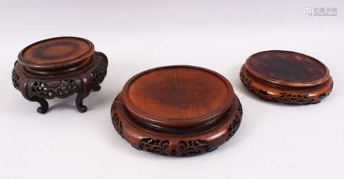 THREE CHINESE HARDWOOD CIRCULAR STANDS, One with curving legs, for vases 7.5