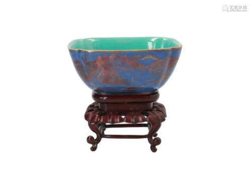 A square blue glazed porcelain bowl on wooden base, decorated in gold with a mountainous