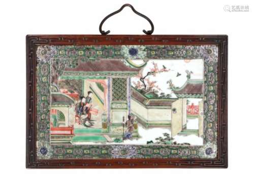 A famille verte porcelain plaque in wooden frame, decorated with figures in a pagoda and garden.