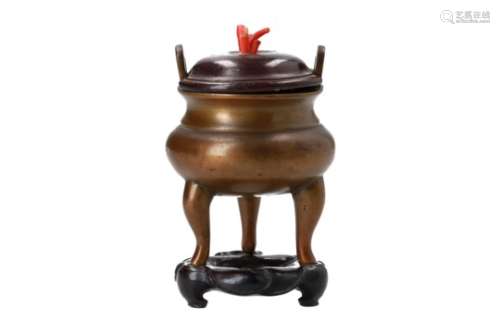 A bronze tripod censer with two handles and a wooden lid with red coral grip, on wooden base.
