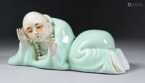 A 20th Century Chinese celadon glazed porcelain reclining figure by Fang Wangsheng, holding an