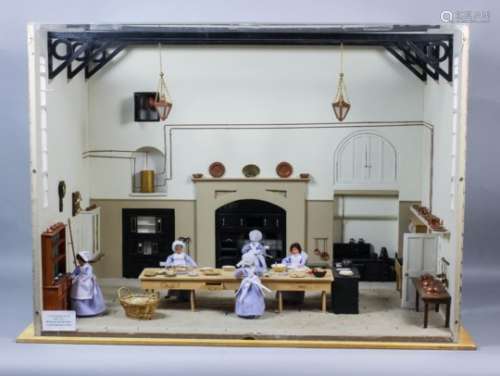 A cased painted wooden model of the interior of a Victorian kitchen showing figures preparing a