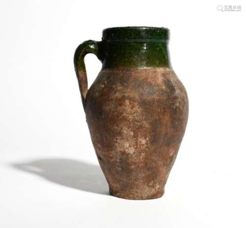 An early earthenware jug probably 15th or 16th century, the reddish body decorated with a green lead