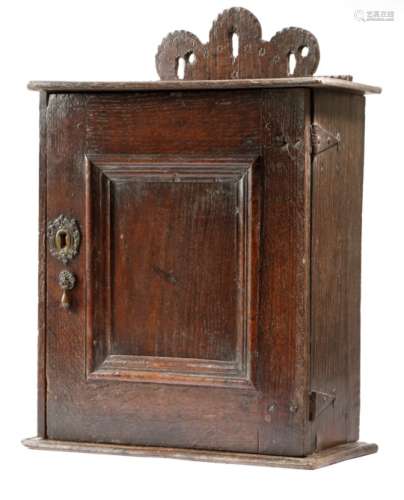 An oak hanging spice cupboard, the raised pierced back with carved and stamped decoration, above a