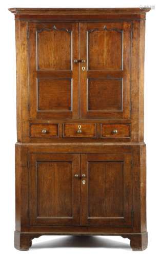 A George III oak standing corner cupboard, with a mahogany frieze, above a pair of arc d'arbelète