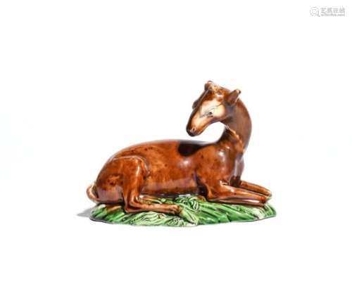 A Brameld creamware figure of a deer c.1800, recumbent on a grassy base, her head turned back over