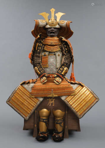 A large gilded Japanese ōyoroi with orange cords (hi’ito odoshi yoroi). A large hoshikabuto-helmet with gilded parts, large fukikaeshi