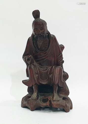 Chinese hardwood sculpture of an Immortal, modelled seated on pierced rockwork holding a bag, 18cm