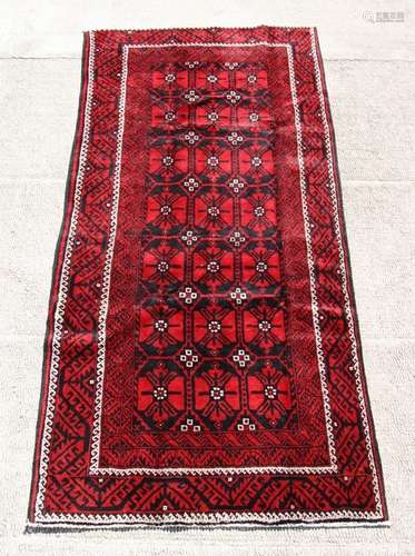 A Persian Baluch woollen hand made rug with repeated guls within a stylised border, on a red ground,