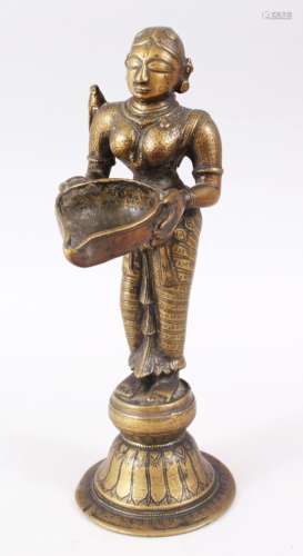 AN 18TH CENTURY INDIAN BRONZE OIL LAMP FIGURE OF LAKSHMI, stood on plinth holding a dish, 27cm