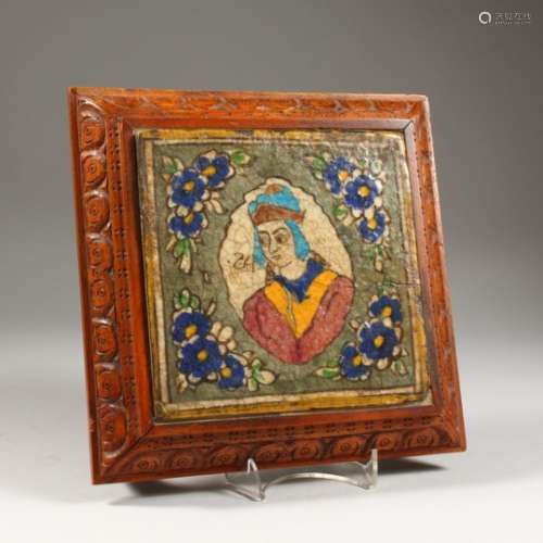 AN ISLAMIC POTTERY TILE, painted with a bust within a floral border, mounted in a later carved