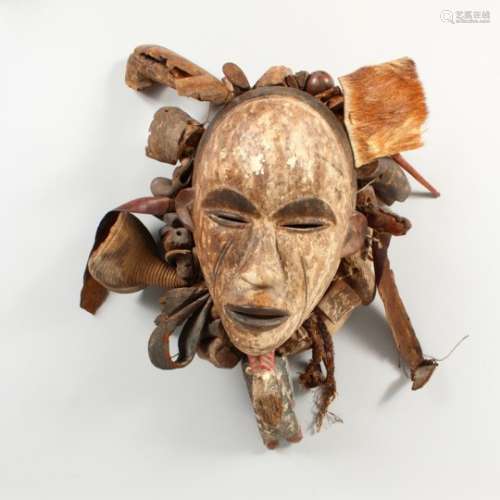 A CARVED AND PAINTED TRIBAL MASK, adorned with various objects, with a lined interior. 20ins high.