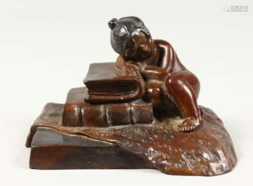 A SMALL CAST BRONZE MODEL OF A YOUNG GIRL ASLEEP AGAINST A PILE OF BOOKS. 5ins wide.