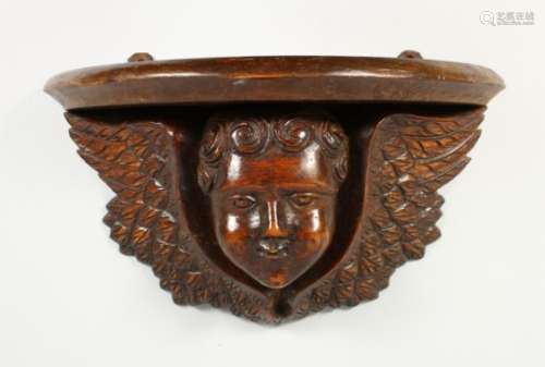 A WOODEN WALL BRACKET, carved as a winged cherub head. 13.5ins wide.