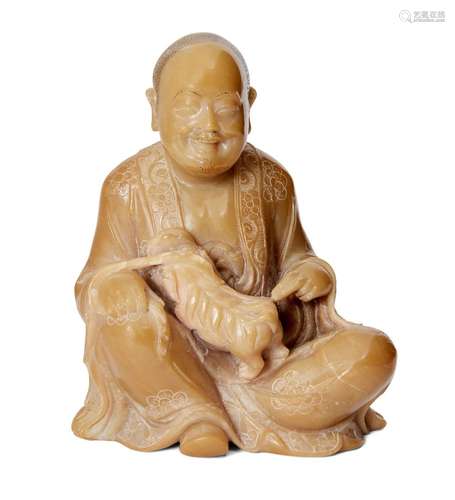 A Chinese soapstone figure of a Luohan, 18th/19th century, carved seated holding a Buddhist lion,