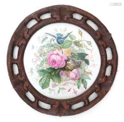 A round porcelain plaque in a carved Schwartzwald frame, decorated with two birds near a nest