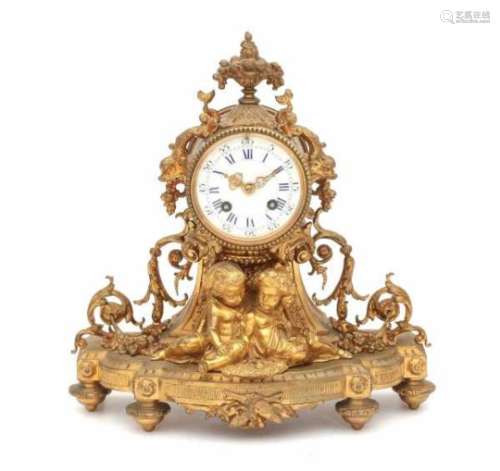 A richly decorated gilt mantle clock with two children sitting on the base. The clockwork with
