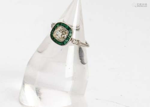 An emerald and diamond Art Deco style dress ring, the cushion cut diamond surrounded by a band of