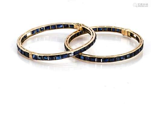 A pair of yellow metal and sapphire bangles, the channel set rectangular sapphires, some vacant