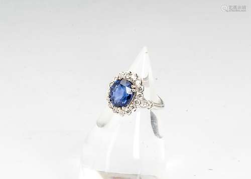 A sapphire and diamond cluster ring, the oval claw set mixed cut sapphire surrounded by a bezel of