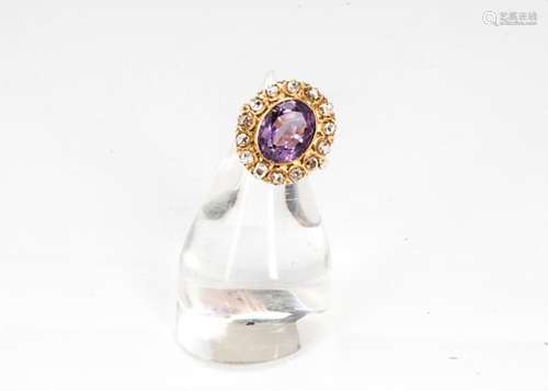 An amethyst and diamond cluster ring, the oval cut central amethyst surrounded by a bezel of rough