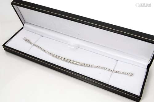 A white metal graduated diamond tennis bracelet, the brilliant cuts in four claw settings with box