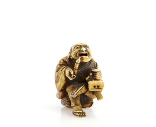 A stained ivory netsuke of a seated man, smoking a pipe whilst holding a sagemono in his left