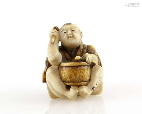 A small stained ivory netsuke of a boy beating a drum, the himotoshi beneath his feet, 19th or