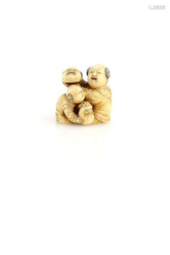 An ivory netsuke carved as two boys with an Okame mask and a Daruma doll, two kanji on the base,