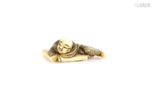 A stained ivory netsuke of a boy lying on two open scrolls, 4.5 cm longProvenance: The Property of a