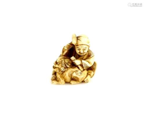 A stained ivory netsuke carved as a seated artisan sculpting a karashishi with hammer and chisel,