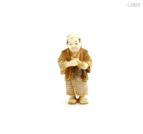 A stained ivory netsuke of a standing man, holding a pipe and pipe case, signed Kozan, 20th