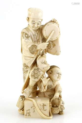 A stained ivory okimono carved as a standing entertainer beating a drum and balancing a kitsune mask