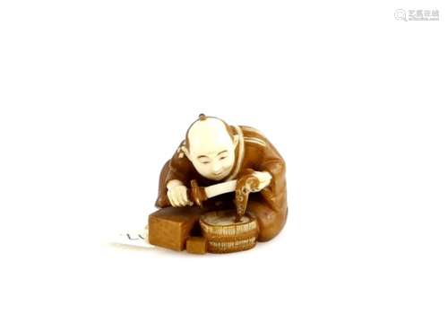 A stained ivory netsuke of a seated swordsmith or polisher, holding a wakizashi; 20th