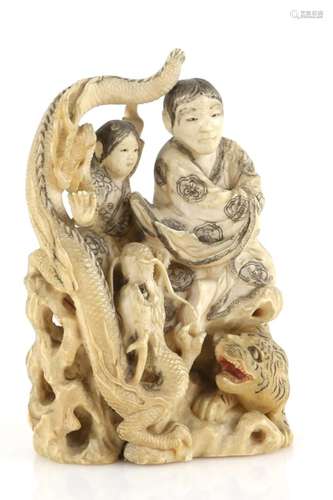 A stained ivory okimono carved as a man and boy beside a dragon and tiger, 12 cm high, signed