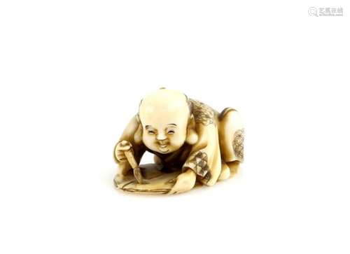 A stained ivory netsuke of a crouching Fukusuke, or other character, practising his calligraphy,