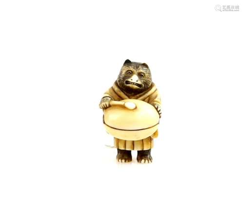 A stained ivory netsuke carved as a Tanuki bear banging a large mokugyo, 19th or 20th