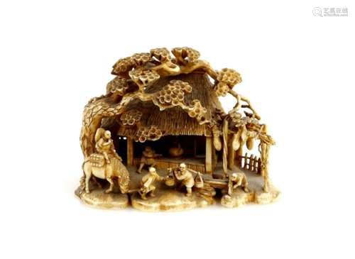 A stained ivory okimono carved as a thatched cottage with figures and pine trees, 8 cm diameter,