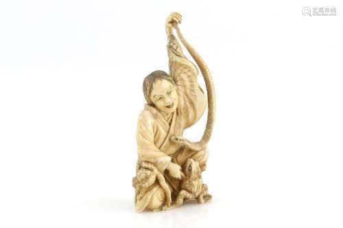 A stained ivory okimono, carved as a seated Sennin holding up a snake with the left hand; a frog