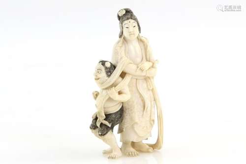 A stained ivory okimono, carved as a standing figure trapping an Oni with a scarf, 8.5 cm high, 20th