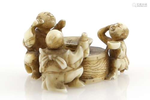 A small stained ivory netsuke of three sake tasters, seated beside a large sakazuki, 19th or 20th