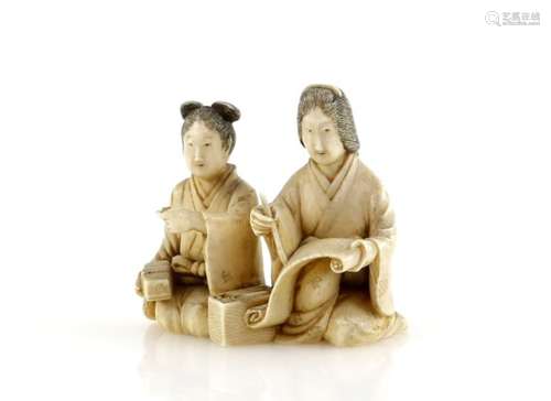 A small stained ivory okimono carved as a man and women writing calligraphy on a makemono, 4cm wide,