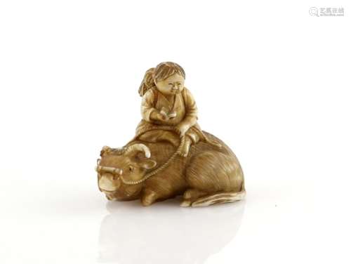 A stained ivory netsuke of a boy reading a text on the back of recumbent water buffalo, 20th