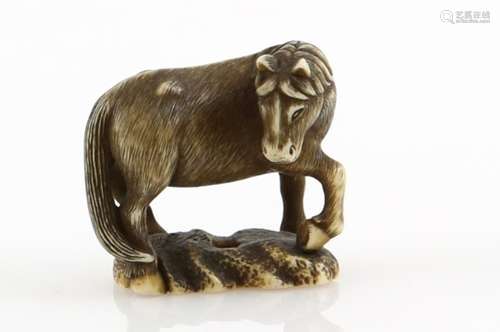 A heavily stained ivory netsuke, carved as a grazing horse looking to the right, signed