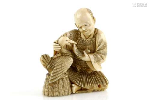 A stained ivory okimono, carved as a cormorant fisherman feeding his bird, nearly 8 cm high, 19th or