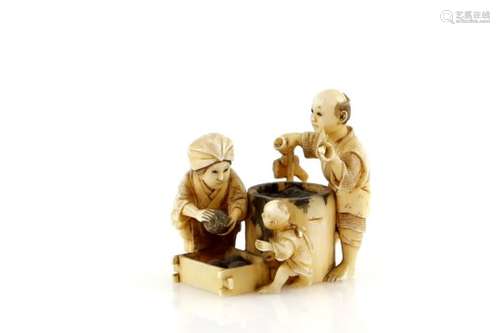 An ivory netsuke or small okimono, carved as a small family making rice balls; the man with a pipe