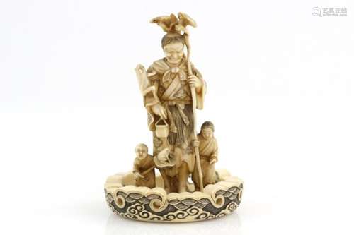 A stained ivory okimono carved as Gama Sennin, holding a staff in his left hand and flanked by two