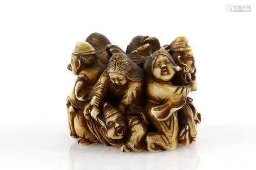 A stained ivory okimono, carved as a group of figures painting each other, 4.5 cm diameter, signed